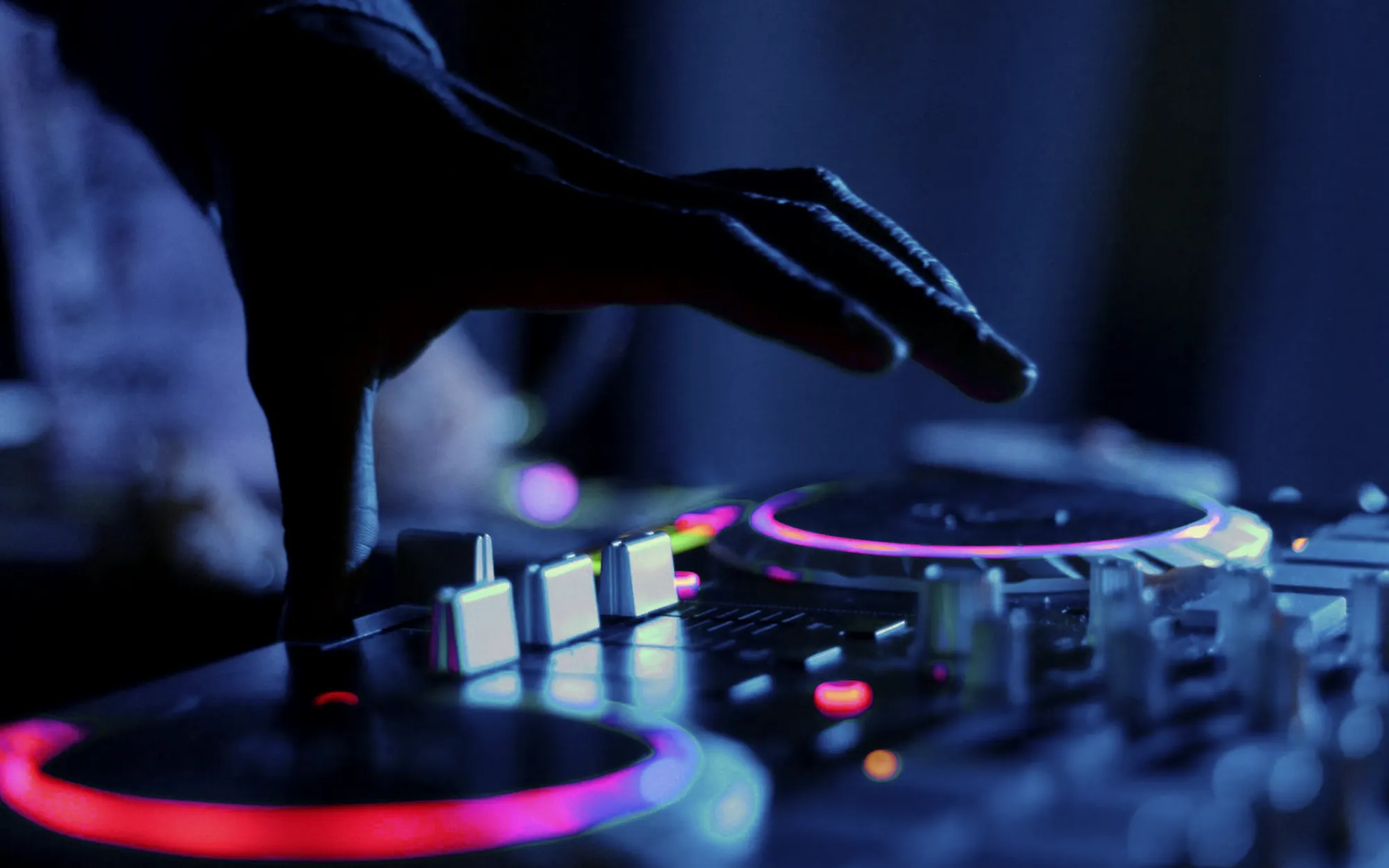 Main d'un DJ au-dessus du jog wheel d'une platine, en lumière de club